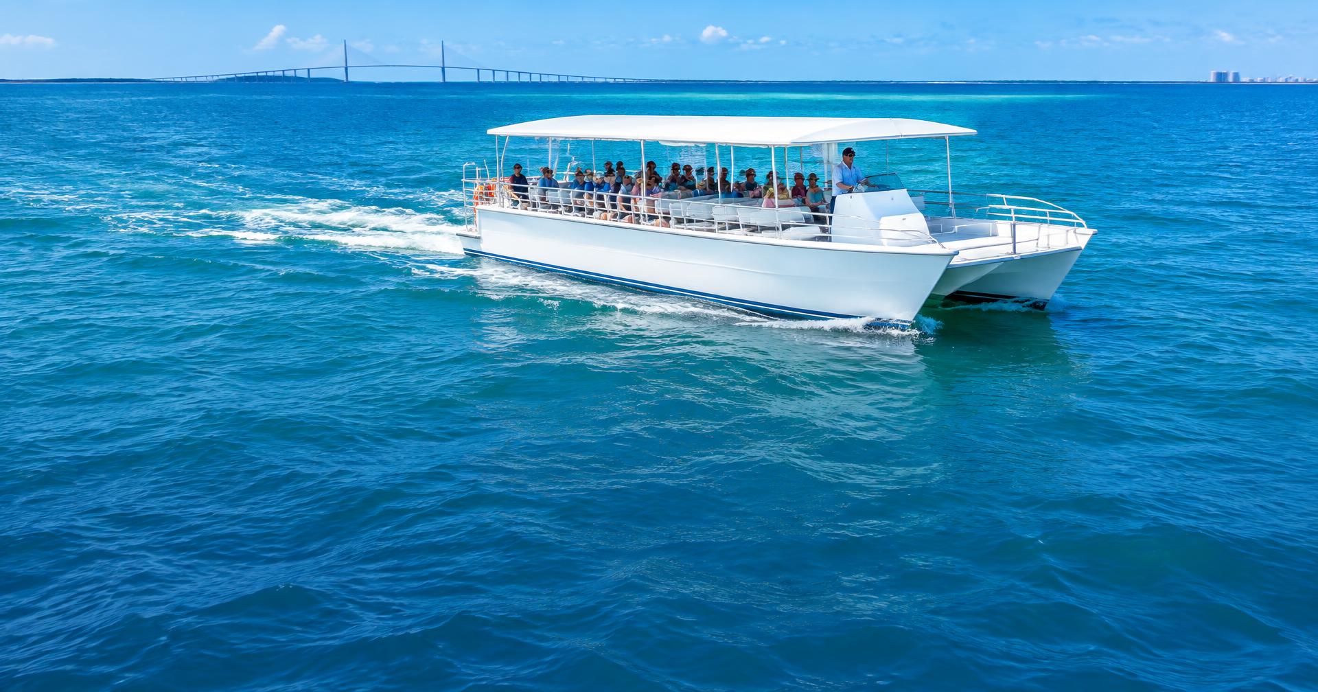 Commercial passenger tour catamaran underway on blue-green Gulf waters, with the Sunshine Skyway in the distance